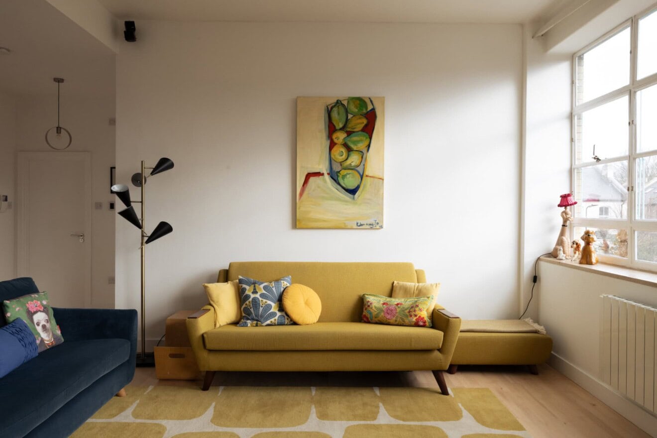 Modern living room with yellow sofa, colourful cushions, and large window in Hackney, London.